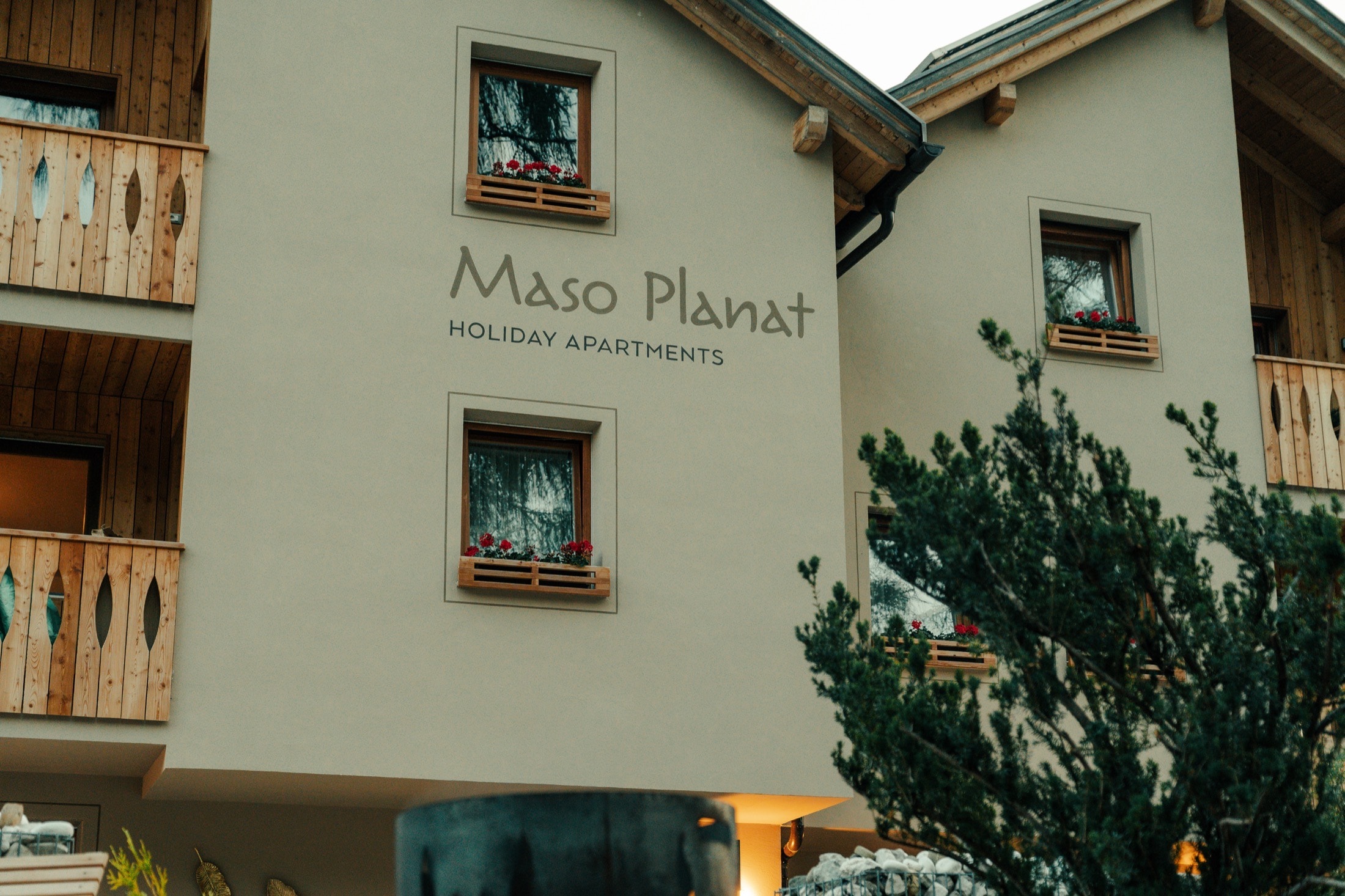 Facciata di Maso Planat con insegna, legno e giardino.