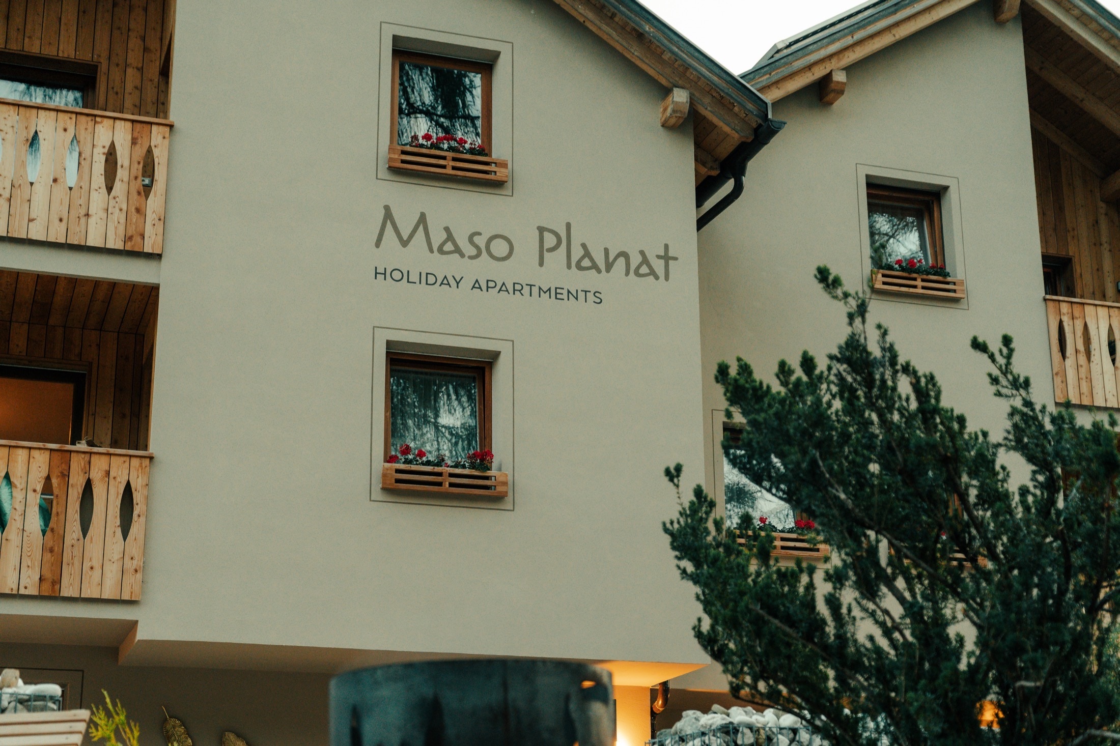 Facciata di Maso Planat con insegna, legno e giardino.